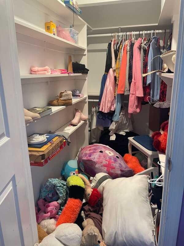 Walk-in closet with clothes, toys and bags piled on the floor before organization